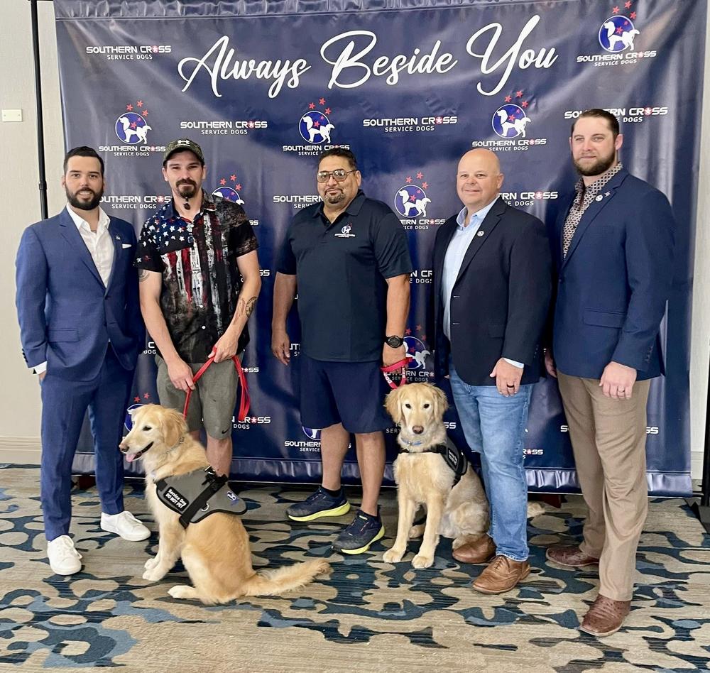 The Southern Cross Service Dogs team standing with three service dogs in front of a banner reading Always Beside You